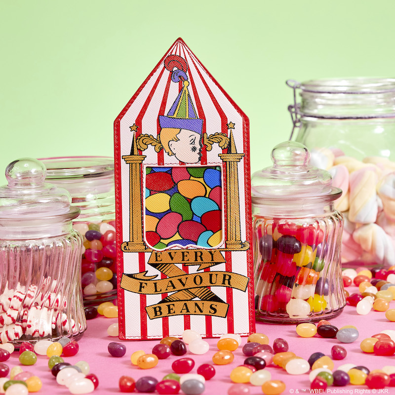 Image of our card holder shaped like a Bertie Bott's Every Flavour Beans container against a pink and green background surrounded by candy